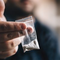 Hand offering ziplock bag filled with white powder