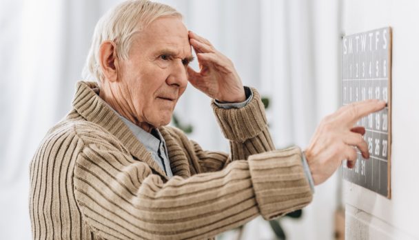 Senior,Man,Looking,At,Wall,Calendar,And,Touching,Head
