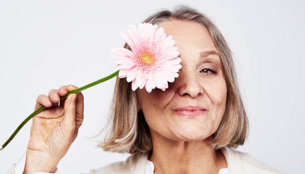 Cheerful,Elegant,Elderly,Woman,Holding,A,Flower,Near,The,Face