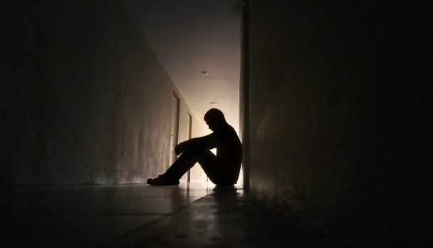 Silhouette,Of,Depressed,Man,Sitting,On,Walkway,Of,Residence,Building.