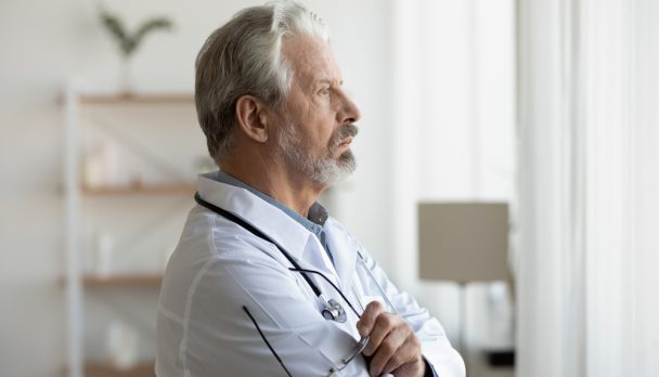 Thoughtful,Serious,Senior,Doctor,Looking,Through,Window,Lost,In,Thoughts.