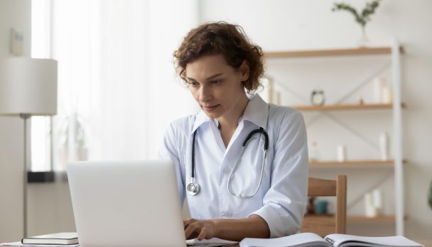 Serious,Woman,Wearing,White,Uniform,With,Stethoscope,Working,On,Laptop,