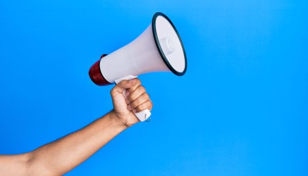 Hand,Of,Hispanic,Man,Holding,Megaphone,Over,Isolated,Blue,Background.