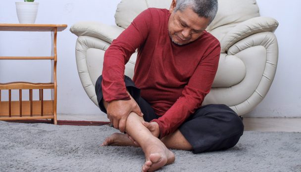 Senior man sitting on floor have cramps in his calves, massage the calf by hands.