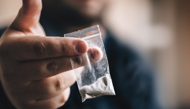 Hand offering ziplock bag filled with white powder